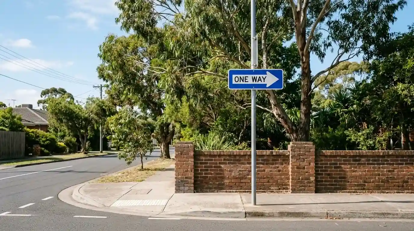 One-way street sign on a quiet suburban corner under clear daylight